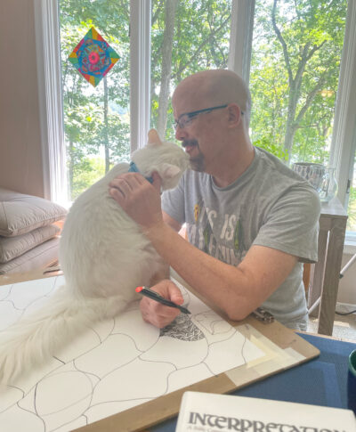 A photo of a man petting a cat that is sitting on his artwork