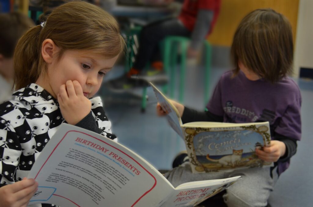 Four panelists, three women and one man, sit on chairs on a stage with a white curtain backdrop during a discussion event. Two water bottles are on a small table between them.