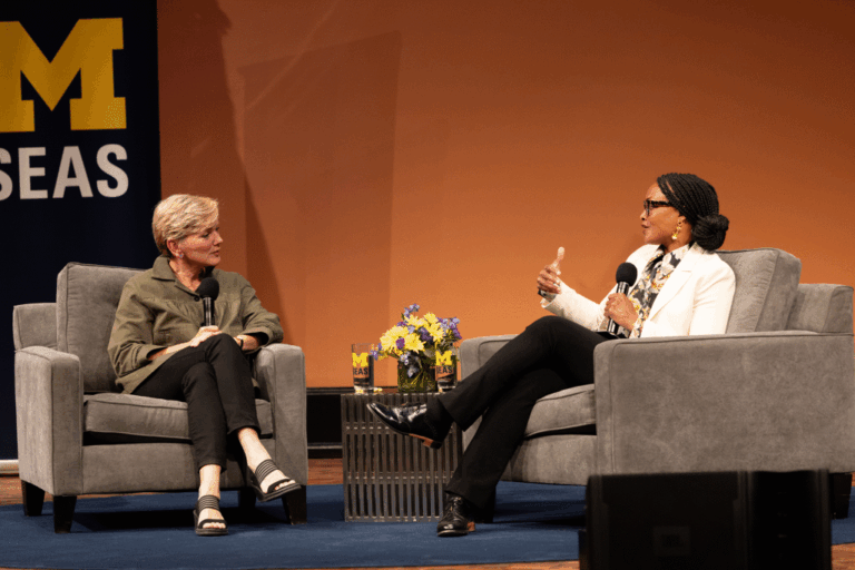 Two women sitting on chairs on a stage with microphones in their hands