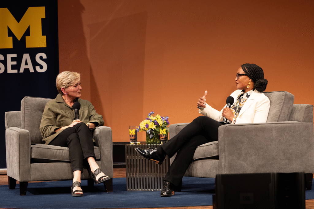 Two women sitting on chairs on a stage with microphones in their hands