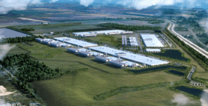 Aerial view of a large industrial complex with multiple long white buildings, surrounded by greenery, roads, and parking areas.