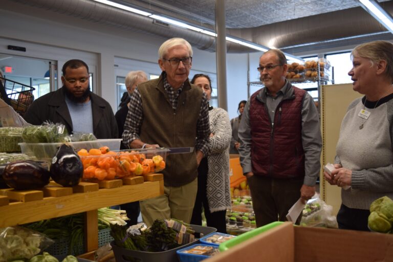 A group of people stand and look at items on store shelves inside a grocery store.