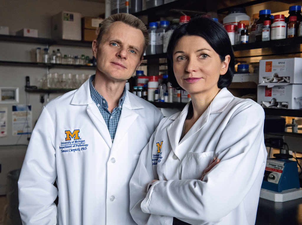 Two people wearing white lab coats stand next to each other