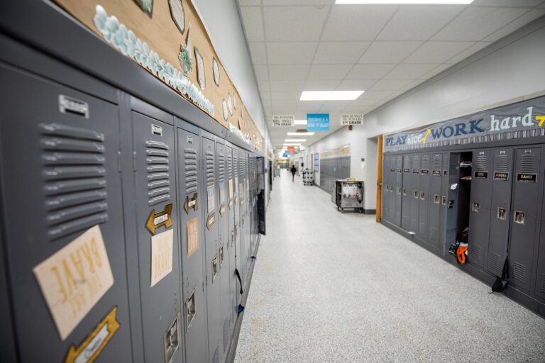 A long school hallway with gray lockers on both sides, motivational signs above the lockers, and a few people visible in the distance.