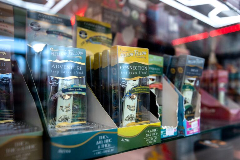Several boxes of Mellow Fellow terp sauce blend vape cartridges are displayed on a glass shelf in a retail store.