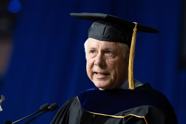 A man wearing a cap and gown speaks at a podium