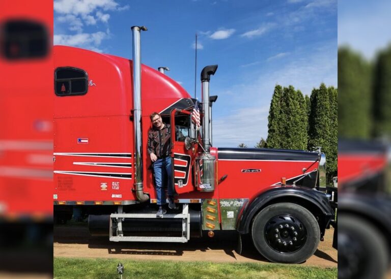 A man wearing a red cap and matching shirt sits on a red riding lawn mower in a grassy field with a dirt path in the background.