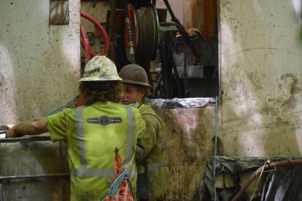A worker operates heavy machinery with hydraulic hoses and metal components in an industrial setting.