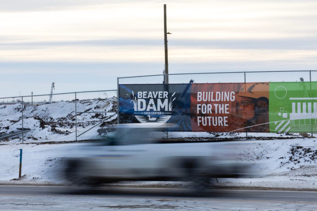 A truck drives past a construction site with a sign reading Beaver Dam Data Center - Building for the Future on a snowy roadside.