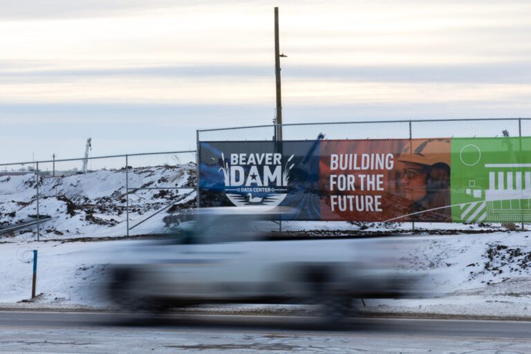 A truck drives past a construction site with a sign reading Beaver Dam Data Center - Building for the Future on a snowy roadside.