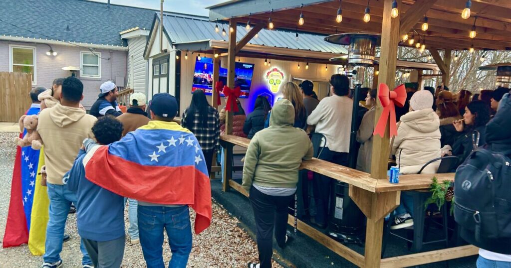 Crowds at The Latin Corner in Pineville watch a Spanish news broadcast of ousted leader Nicolás Maduro arriving in New York in federal custody.