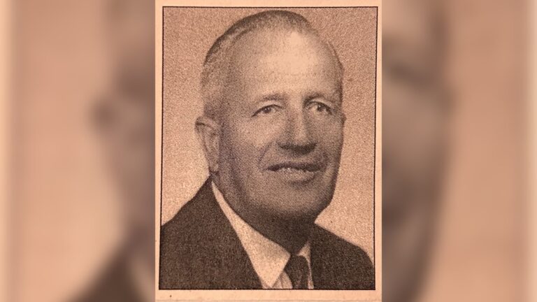 Black and white portrait of an older man wearing a suit and tie, looking at the camera with a neutral expression.