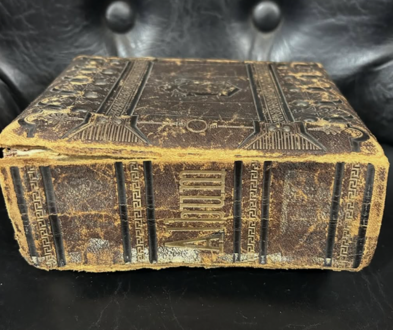 A worn, ornate leather-bound book with embossed patterns and a metal clasp sits on a black tufted leather surface.