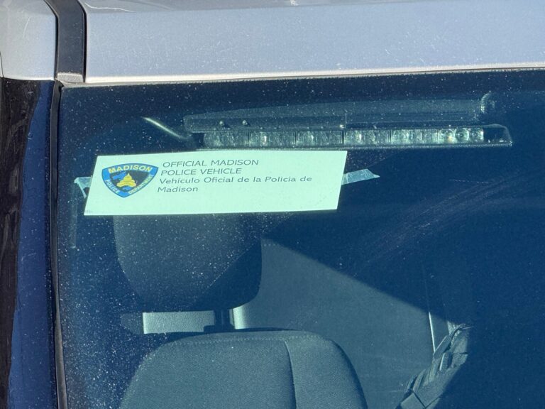 A sign reading Official Madison Police Vehicle is displayed on the dashboard inside a car.
