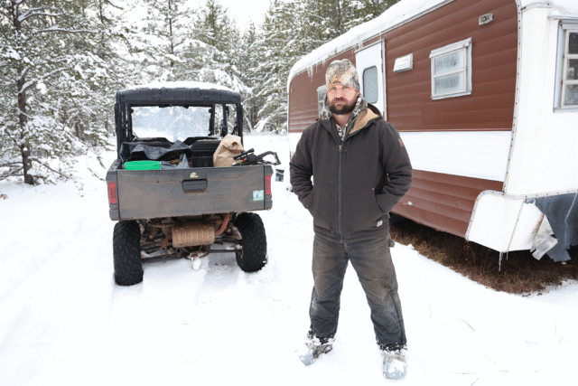 A man stands in front of a hunting camper in the snow