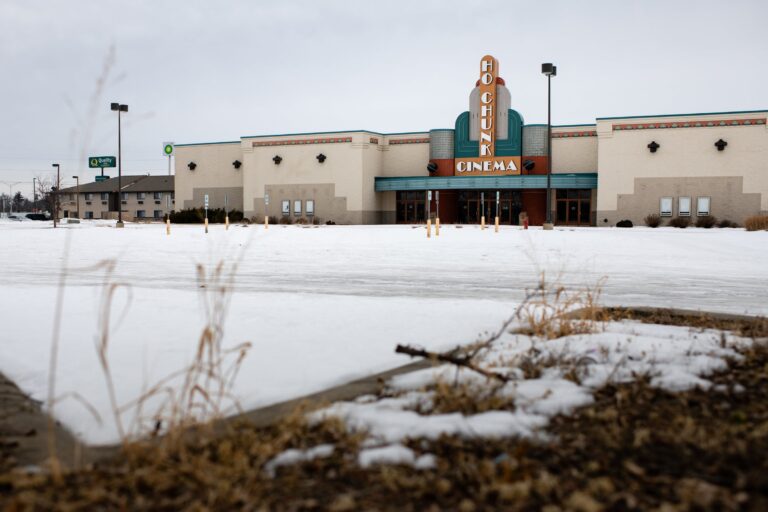 A hand holds a Ho-Chunk Nation identification card displaying enrollment details, photo, name, address, and physical description against a patterned background.