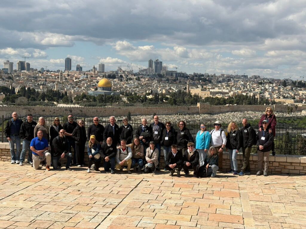 People ascend outdoor stairs and an escalator from an underground area toward a bright blue sky; a bird flies above and a building is visible in the background.