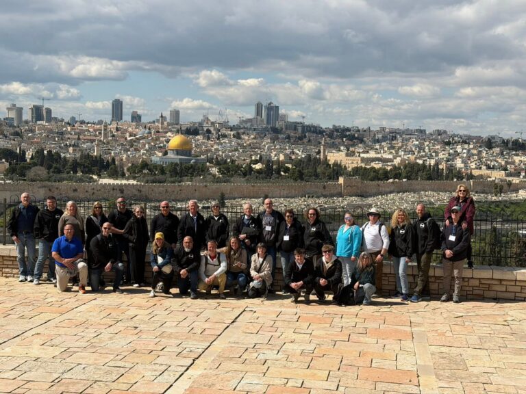 People ascend outdoor stairs and an escalator from an underground area toward a bright blue sky; a bird flies above and a building is visible in the background.