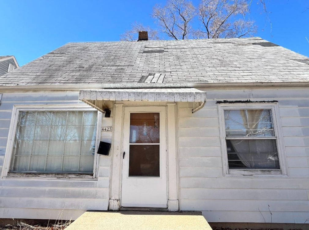 A doorway with a damaged threshold; black tape covers gaps, and the wood is worn and dirty. The door is open, revealing carpet inside and a brick wall on the right.
