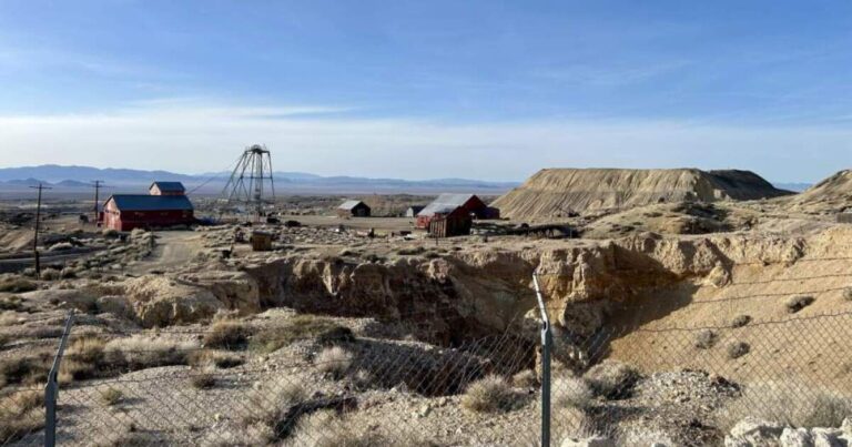 A man sitting outside, looking away from the camera while smiling.