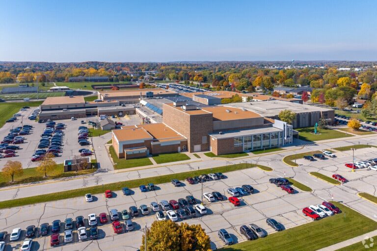 Entrance of West High School with glass doors, large windows, and the school name and mascot displayed on a brick building under a partly cloudy sky.