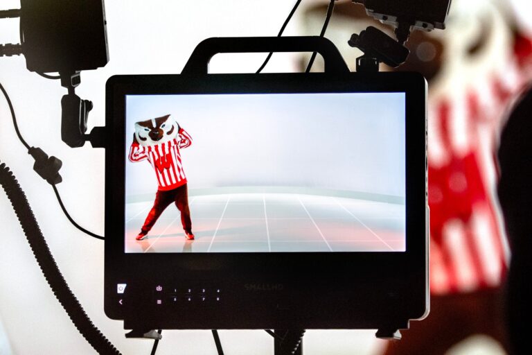 A camera monitor displays a person in a red and white striped outfit and a badger mask posing in a studio with a plain white background.