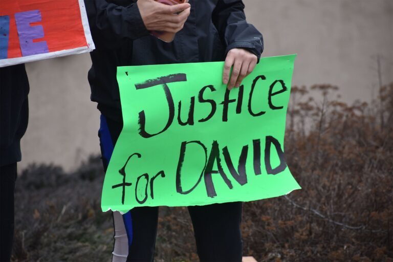 A woman with long dark hair and sunglasses on her head stands outdoors, looking slightly to the side with a neutral expression.