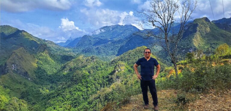 A black-and-white photo of seven children and two women, one holding a baby, with one child holding a sign that reads BV03571. They stand in front of thatched structures.