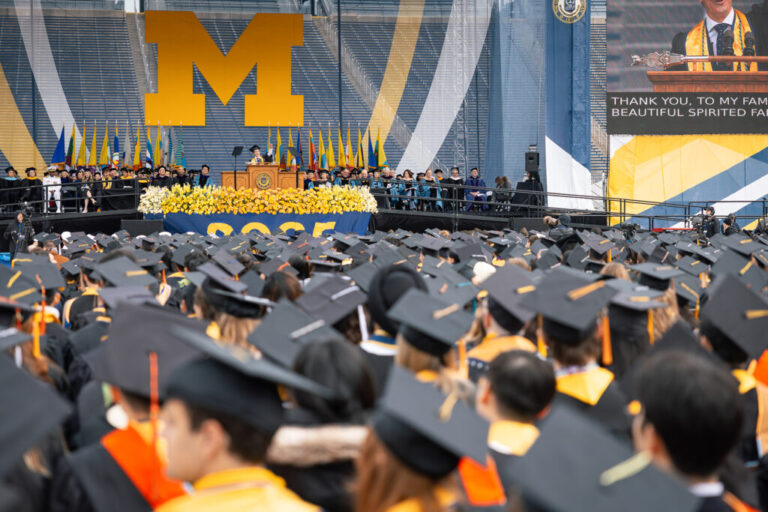 People wearing graduation caps sit facing a stage