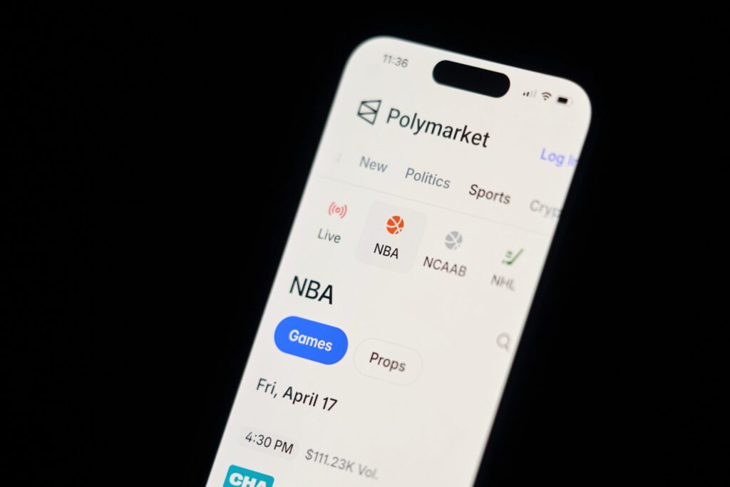 A smartphone screen displays the Polymarket app, showing sports categories and NBA game information for Friday, April 17.