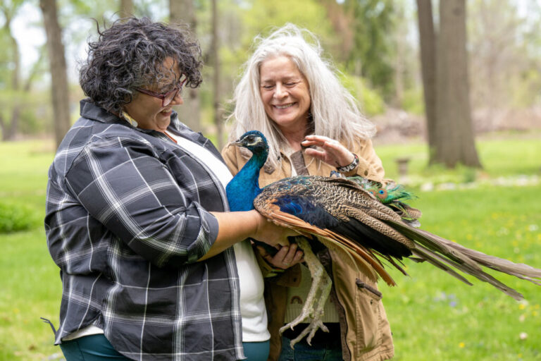 Geila Rajaee (left) and K Rivet Amico, both instructors in the School of Public Health, are shown here with Hero, an 18-year-old peacock.