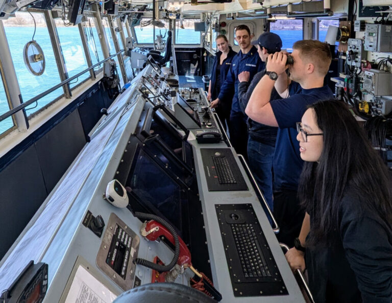 Five people stand at the bridge of a vessel while it is docked