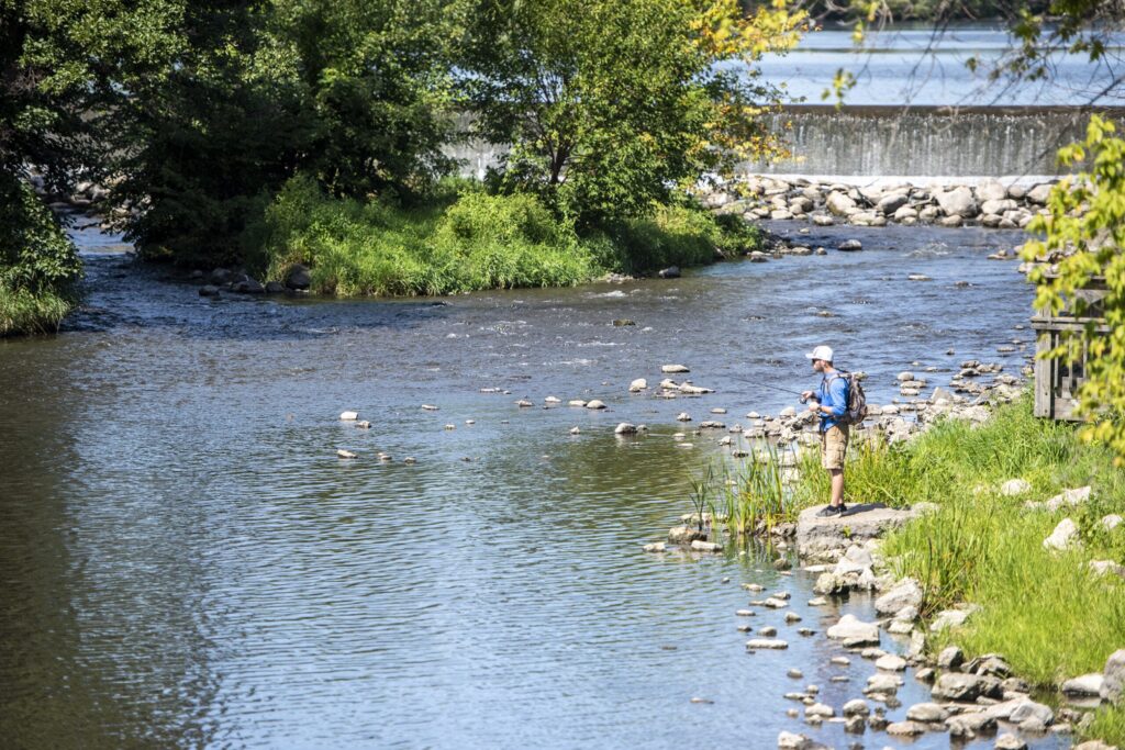 Water streams down a dam behind a fisherman casting a line into the river.