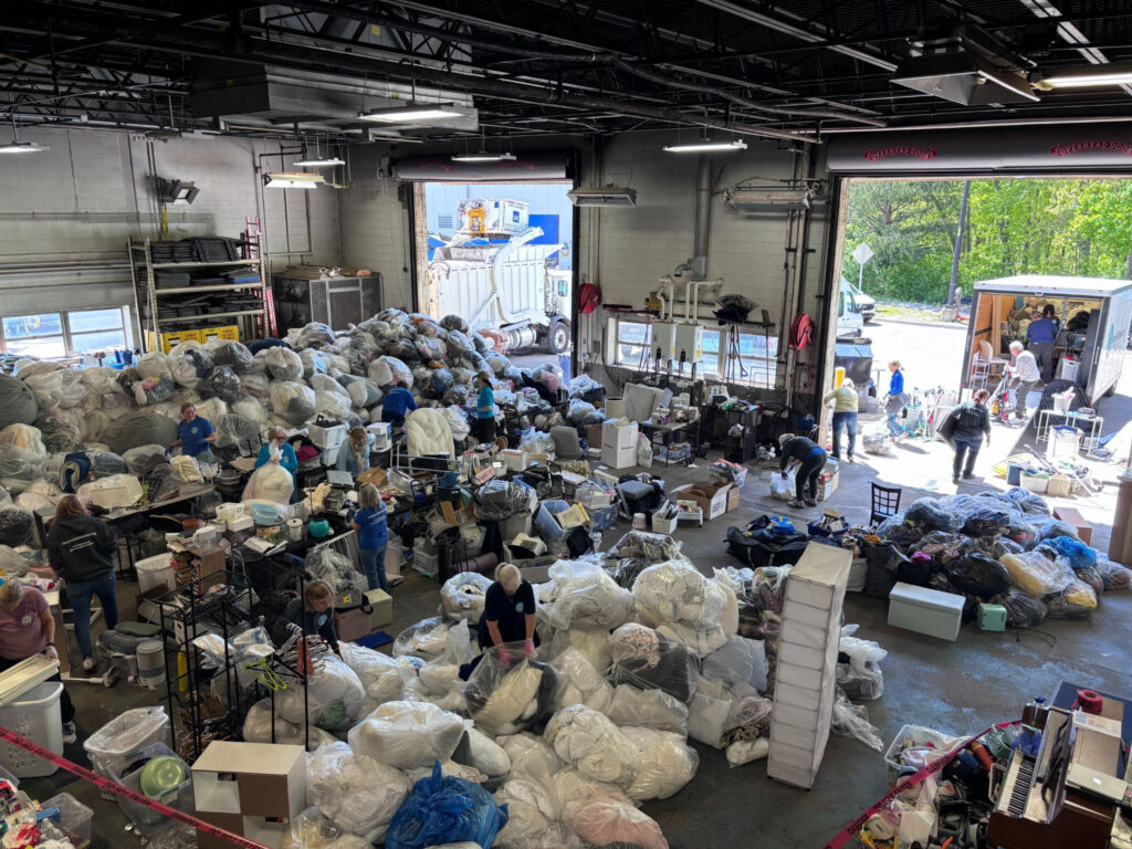 A room full of a bags of clothing and other donations with people milling about