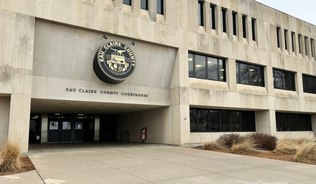 Exterior view of the Eau Claire County Courthouse building with its official seal above the entrance and surrounding concrete and landscaping.