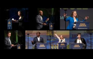 A woman in a blue suit speaks at a podium labeled WISDEMS CONVENTION Save the American Dream with a microphone and outstretched arms.