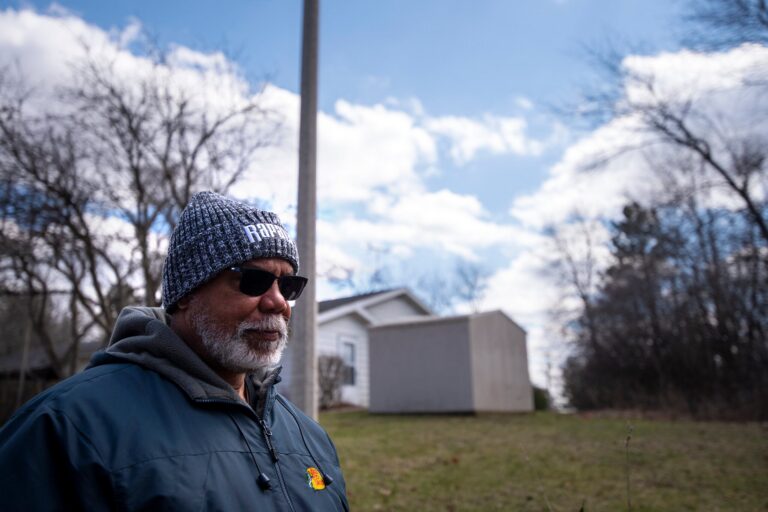 A man walks past small buildings outside.
