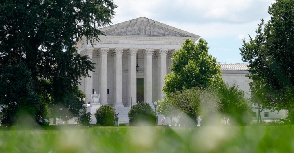 The United States Supreme Court building is seen in the background, partially obscured by green trees and grass in the foreground.