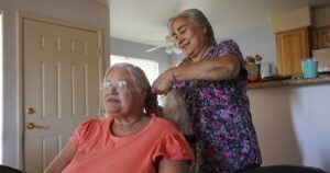 Care worker Irma Luz López, or Malu, embraces her now-former client, Diane Wohlman, in her Las Vegas home on June 21, 2026. Wohlman’s cat, White Socks, lounges in the kitchen.