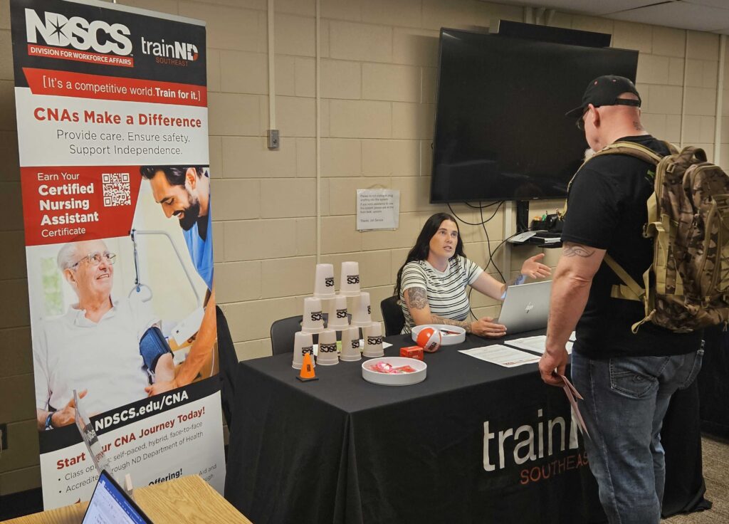 McKenna Melby of the North Dakota State College of Science speaks with a job fair attendee in Fargo, North Dakota, on July 28, 2026. Melby was recruiting potential students for the certified nursing assistant program.(Photo by Jeff Beach/North Dakota Monitor)