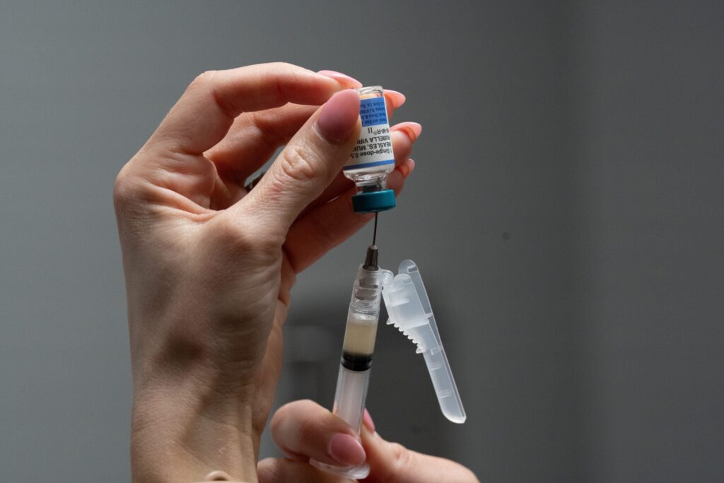 A person holds a vial upside down and draws liquid into a syringe with a needle, preparing for an injection.
