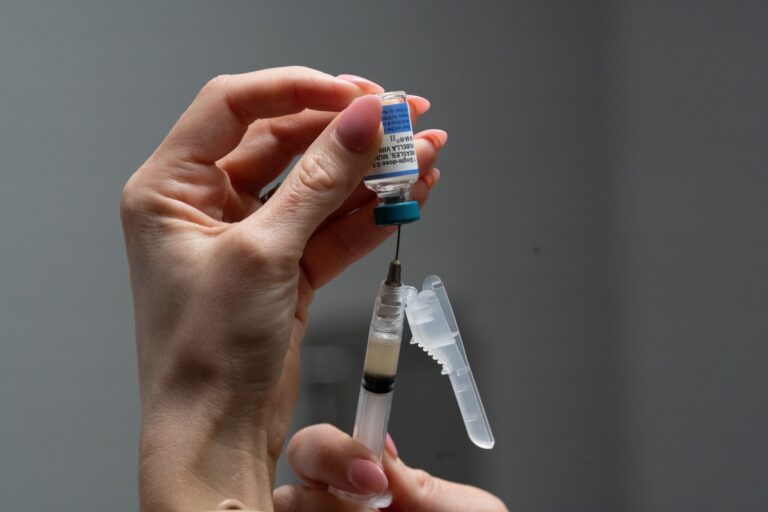 A person holds a vial upside down and draws liquid into a syringe with a needle, preparing for an injection.