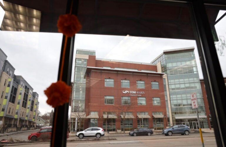 View through a window showing a street and the SSM Health Clinic building with cars parked along the road.