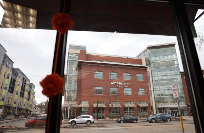 View through a window showing a street and the SSM Health Clinic building with cars parked along the road.