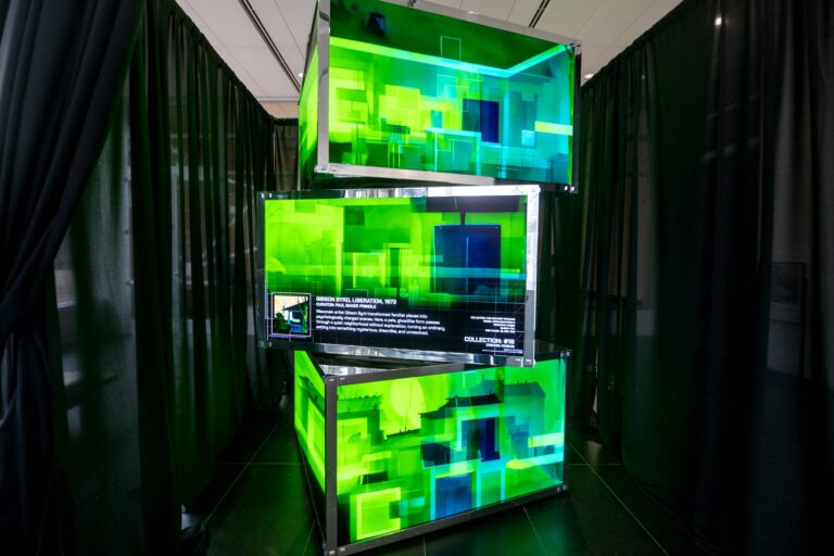 A man stands by an interactive display in front of three illuminated yellow tanks filled with objects.