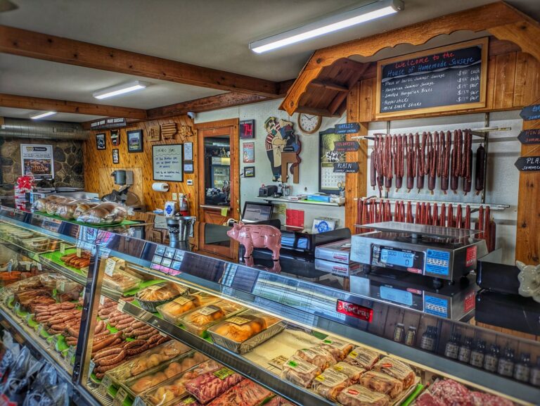 Three butchers in white uniforms stand behind a counter filled with sausages and meats. Shelves of hanging sausages are visible in the background. Text reads: Best of the Wurst.