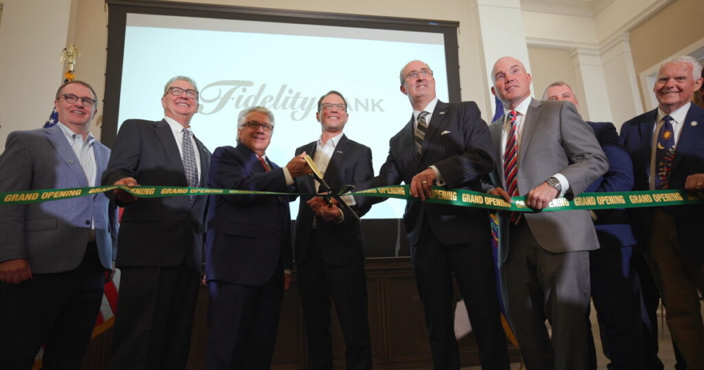 Lackawanna County Commissioner Thom Welby, left, state Rep. Kyle Donahue, state Rep. Bridget Kosierowski, state Sen. Marty Flynn, Brian Cali, chair of the Fidelity Bank Board of Directors; Governor Josh Shapiro and Daniel J. Santaniello, Fidelity Bank President and Chief Executive Officer, watch a video about the renovations to the Scranton Electric Building.