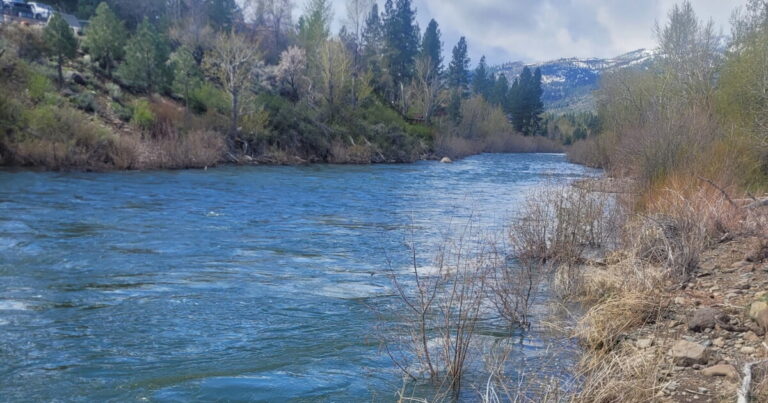 Side-by-side illustration of a river in fall and spring. The spring river is higher and wider, with more microplastic particles shown moving through the water and along the riverbed.